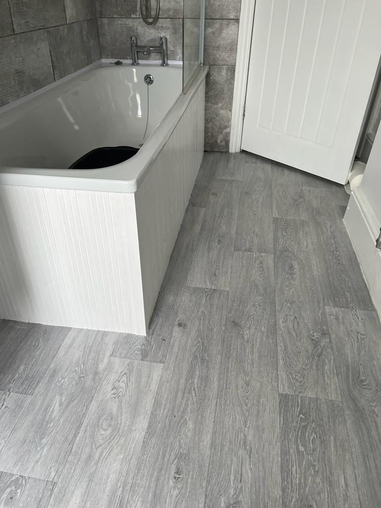 Renovated bathroom with a panelled bath, grey tiling and wood-effect flooring by Plummer's Home Improvements